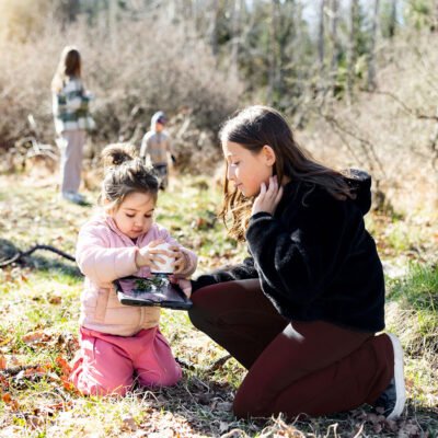 En förskoleelev och en elev på lågstadiet utforska med digitala verktyg i skogen.