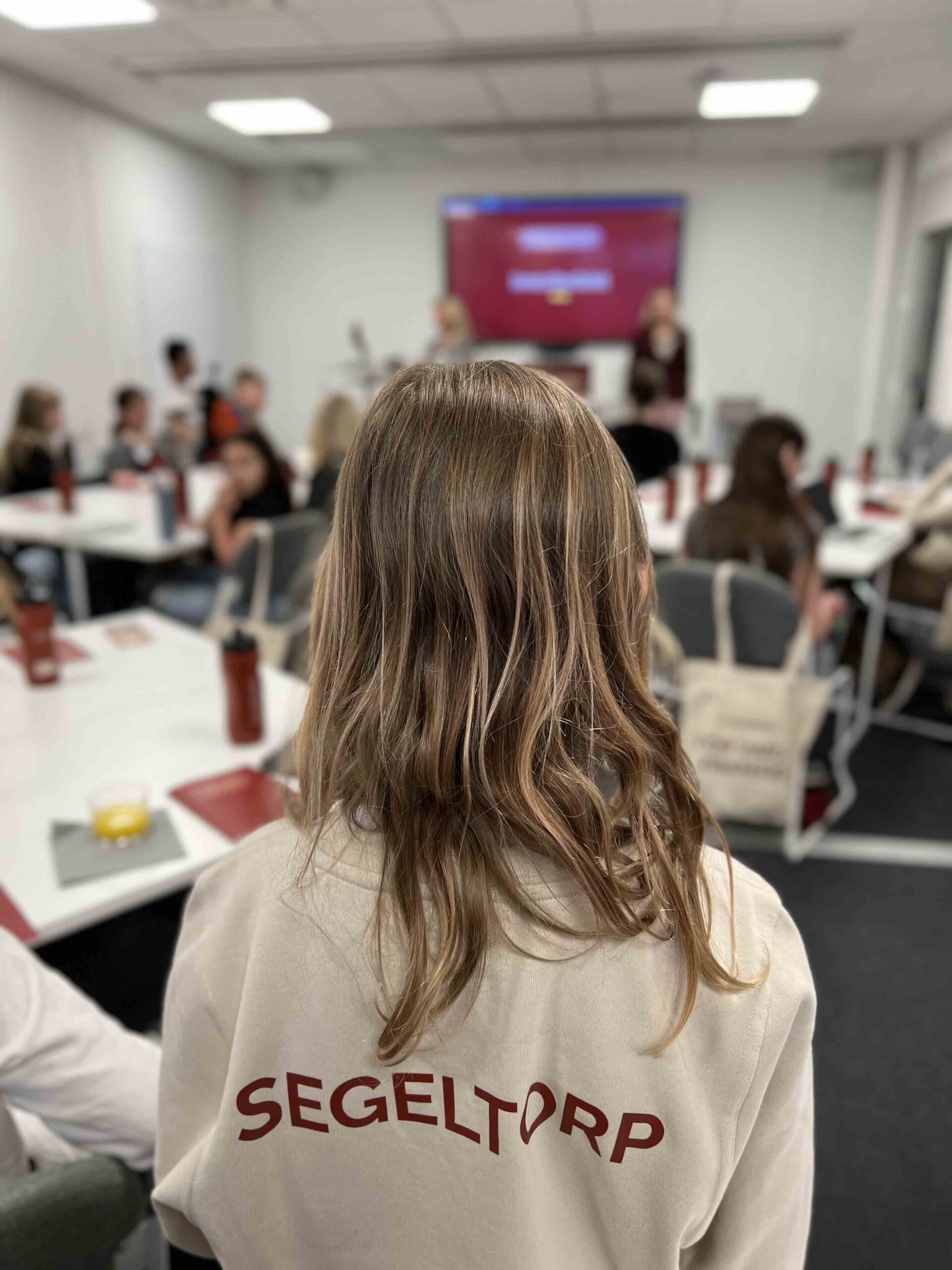 Elev på Innovitaskolan med ryggen mot kameran står i ett rum med flera andra elever, på tröjan står det Segeltorp.