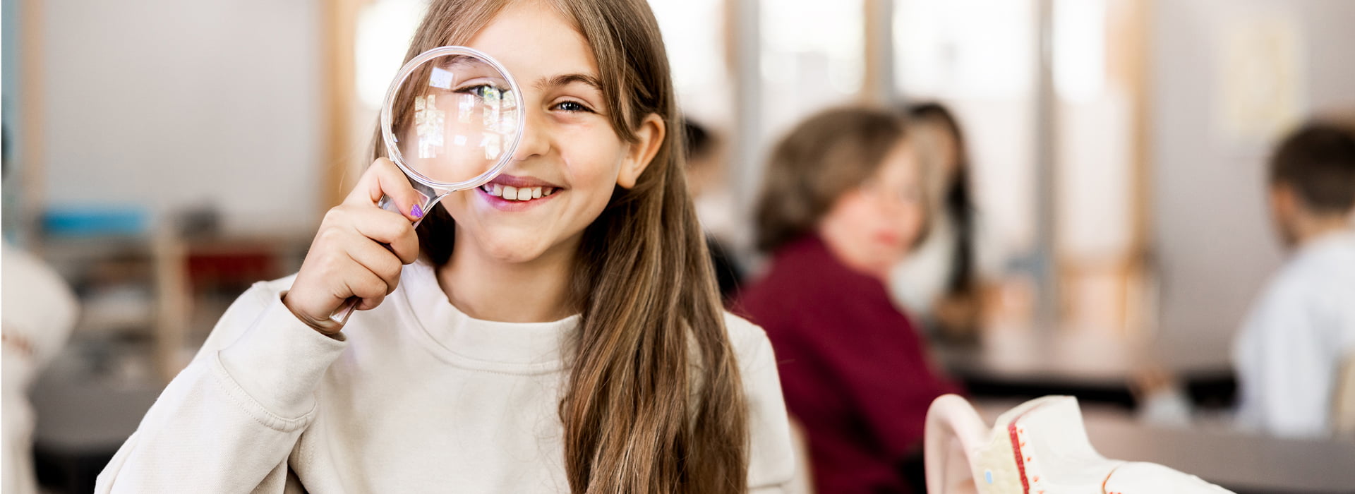 Flicka på Innovitaskolan tittar mot kameran genom ett förstoringsglas.
