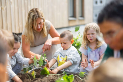 Pedagog hjälper barn att plantera på gården.