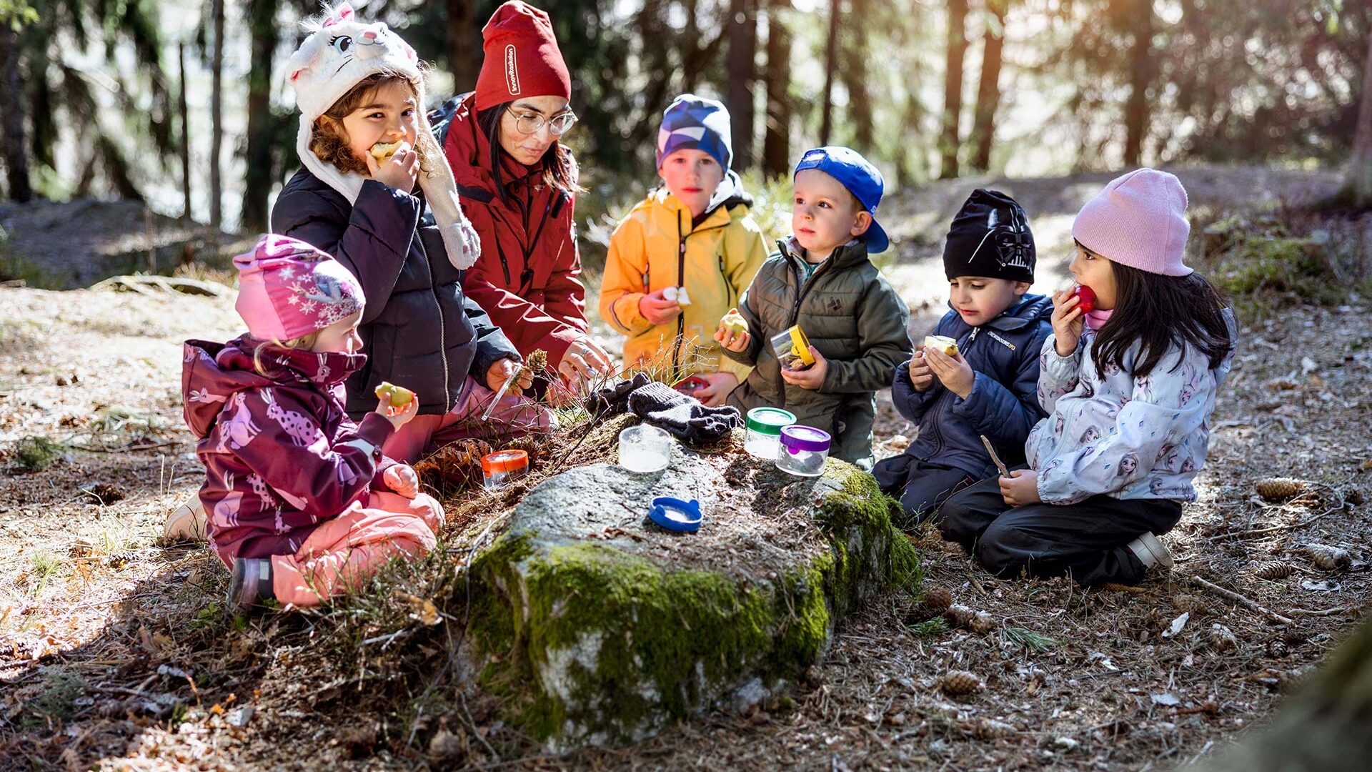 Förskolebarn äter mellanmål ute i naturen.