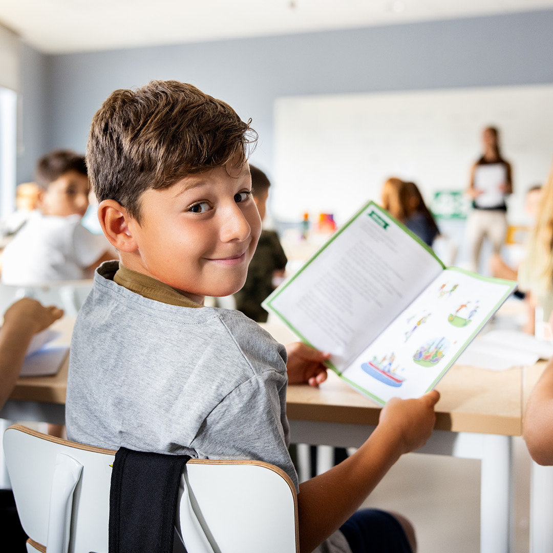 Elev i mellanstadiet tittar över axeln med en bok i händerna i ett ljust klassrum