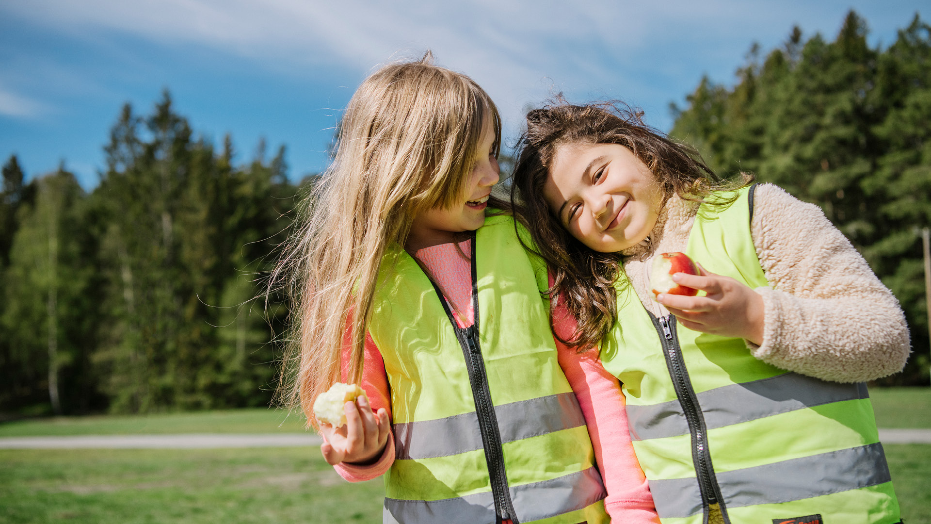 Två glada elever i förskoleklass ute i naturen med varsitt äpple