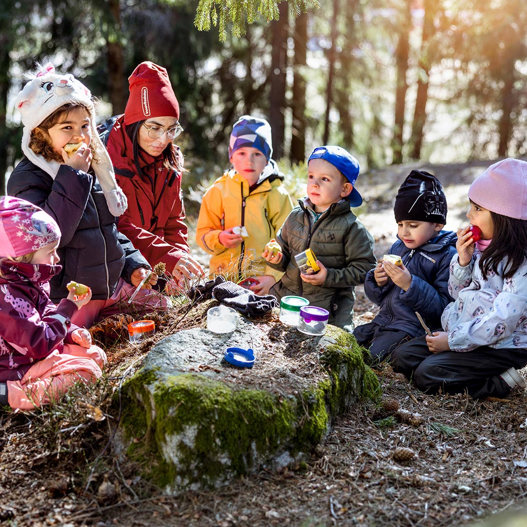 Förskolebarn äter mellanmål ute i naturen.