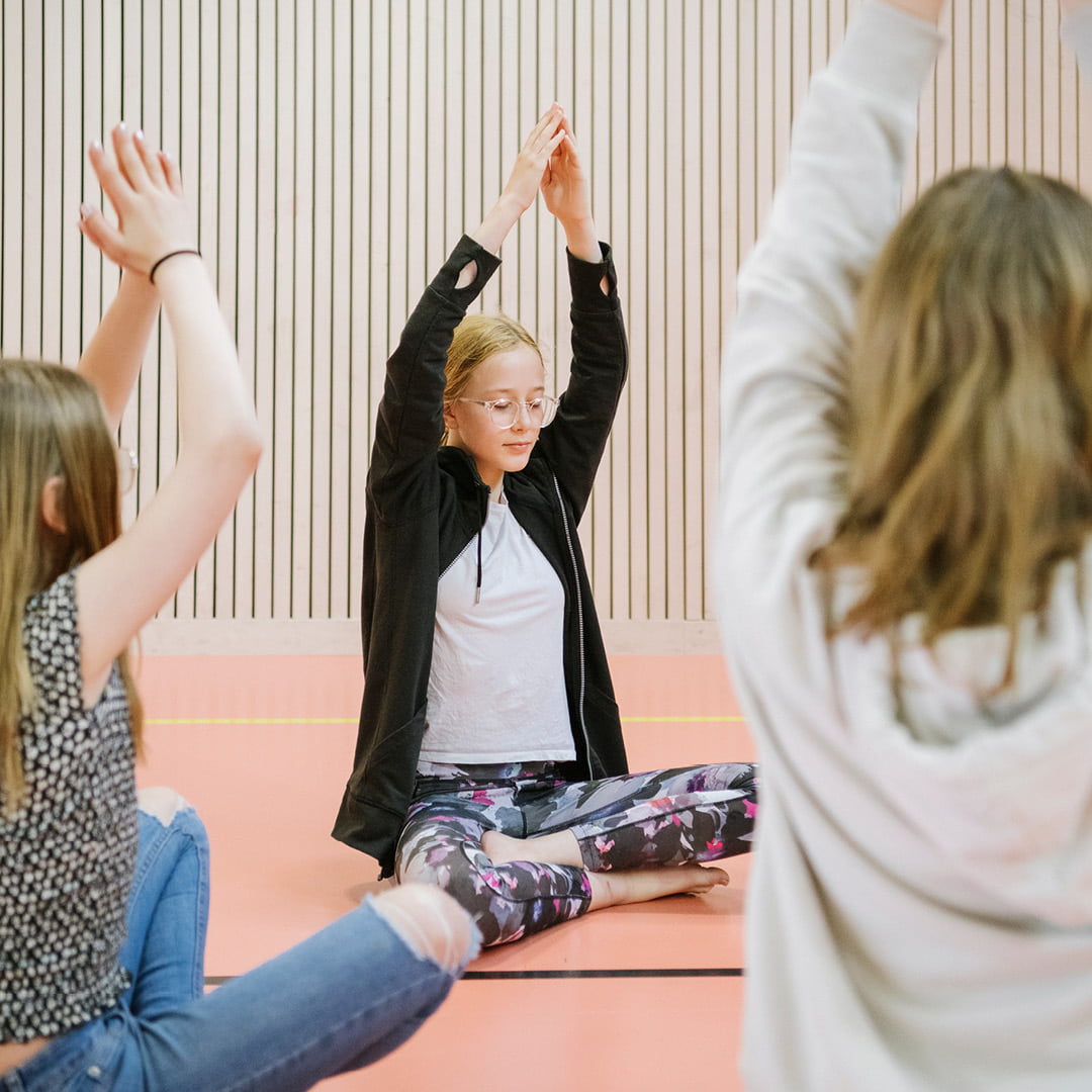 Tre elever i mellanstadiet som utövar yoga i en idrottssal på Innovitaskolan