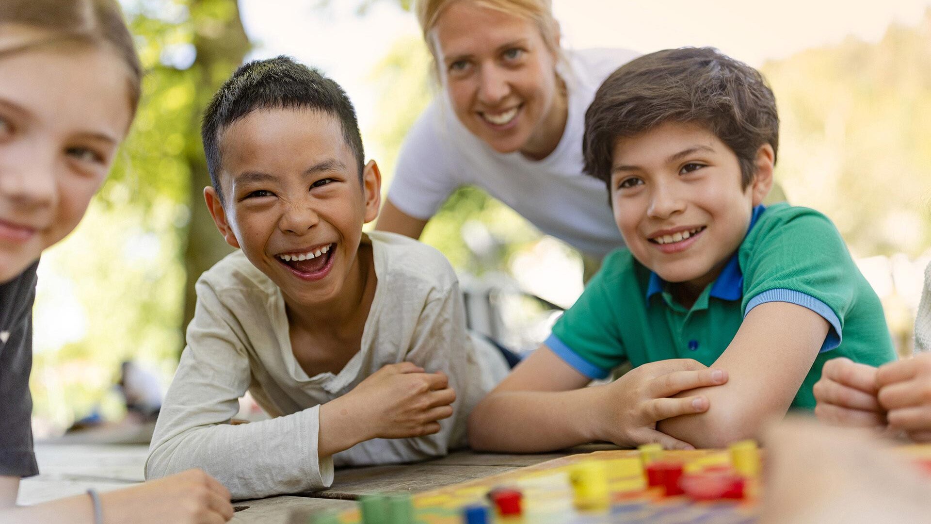 Tre glada elever och en pedagog spelar fia med knuff utomhus.