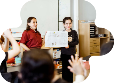 Två glada flickor står framme vid tavlan och presenterar sitt arbete.