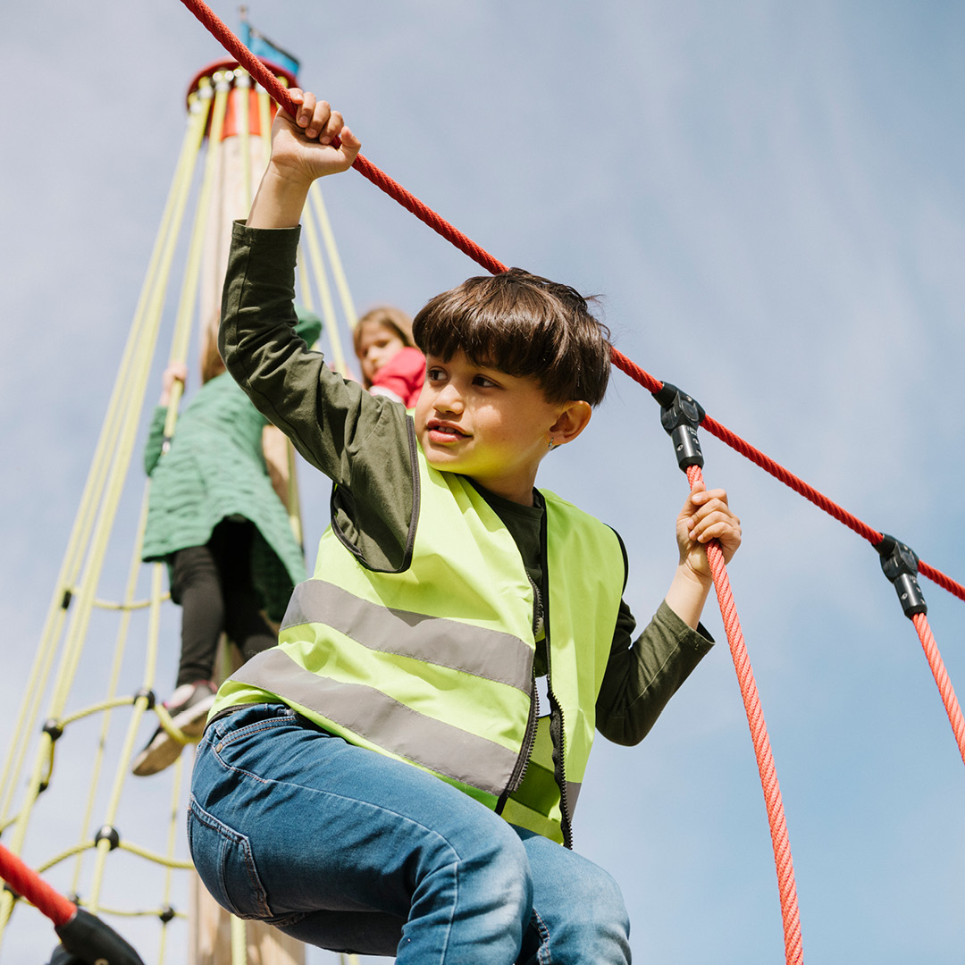 Ett barn i förskoleklass som klättrar på en lekplats