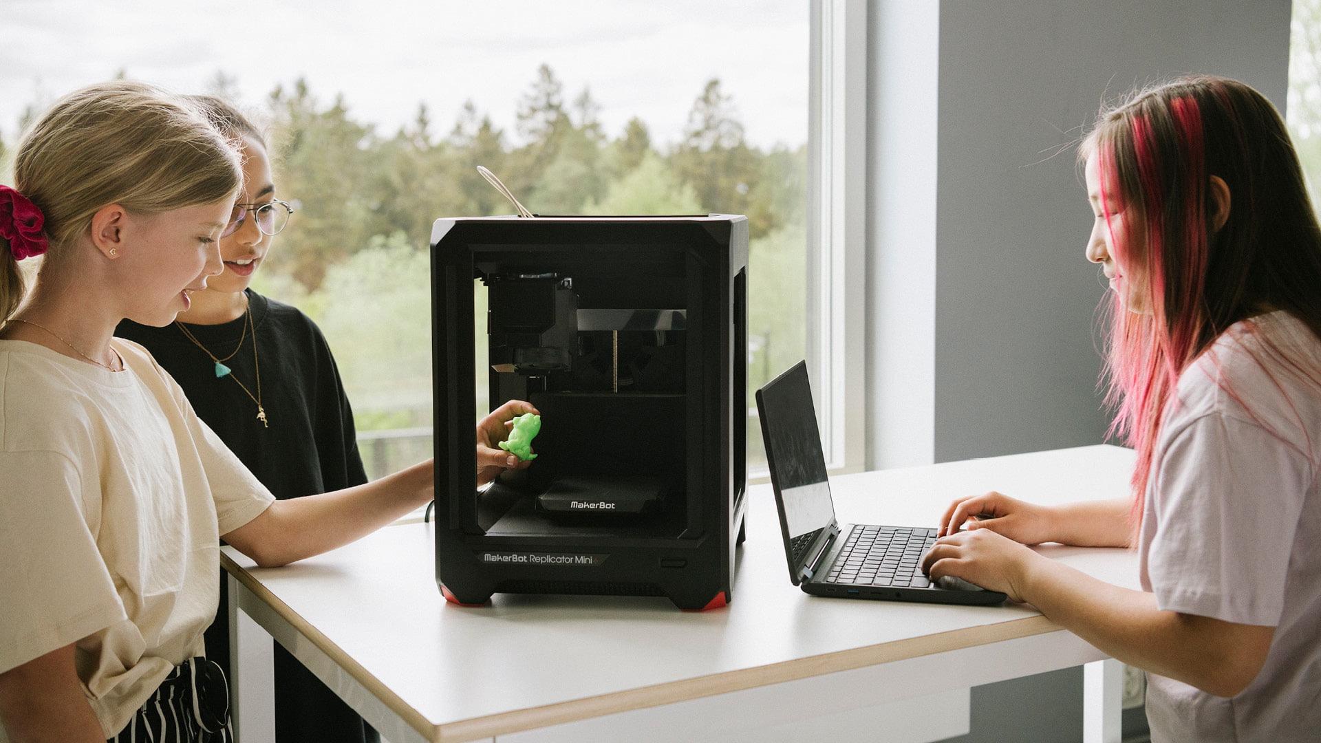 Tre elever arbetar med en 3D-printer och en dator på Innovitaskolan