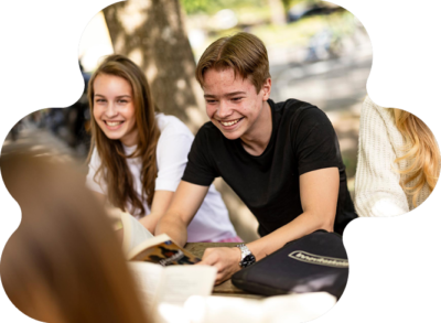 Tre glada elever sitter utomhus på skolgården och skrattar.